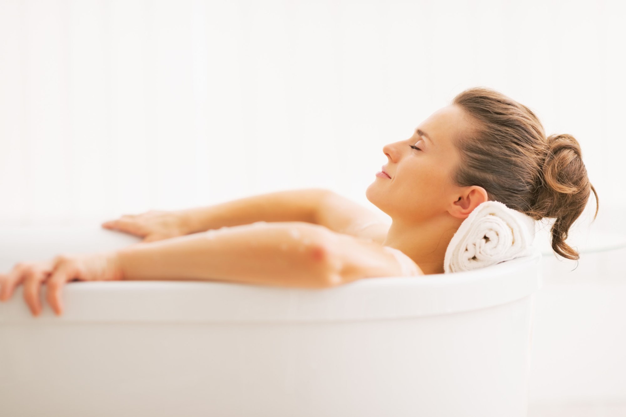 Frau mit langen braunen haaren liegt entspannt in einer Badewanne